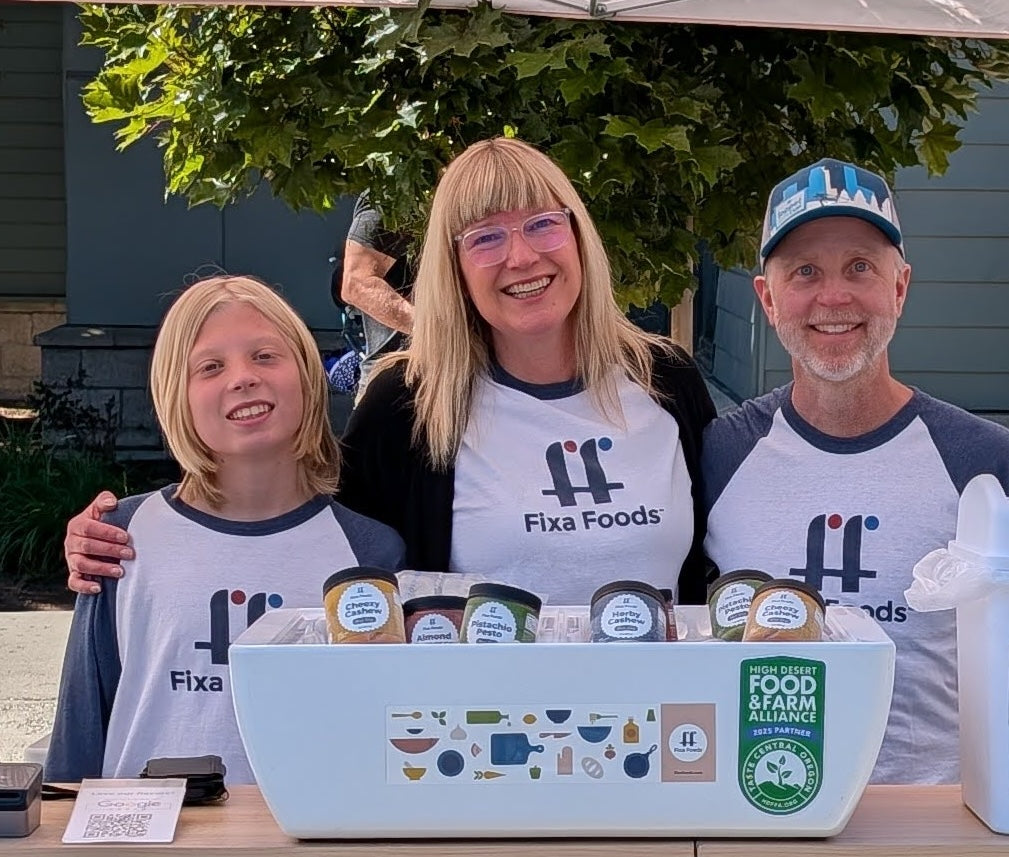 Three people wearing Fixa Foods shirts standing behind a display ofFixa Foods products.